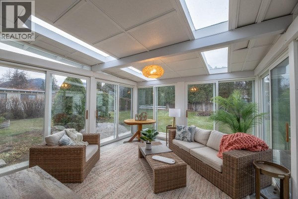 Bright sunroom with glass walls, wicker furniture, and a round table, overlooking the backyard. - 5214 Nixon Road, Summerland