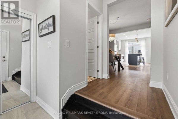 Entryway hallway with light grey walls, wood floors, and open view into the kitchen and dining area. - 522 Culdaff Road, Ottawa