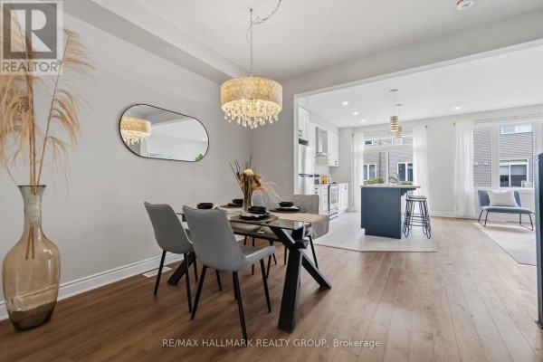 Dining area with glass table, grey chairs, and crystal chandelier, open to kitchen and living space. - 522 Culdaff Road, Ottawa