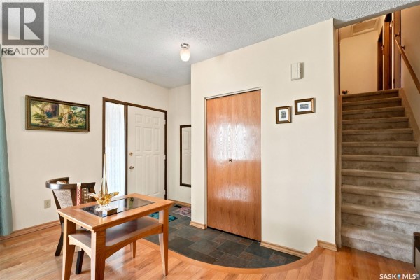 Interior view of a home's entryway with a small dining table, front door, closet doors, and a staircase. - 522 Delaronde Road, Saskatoon