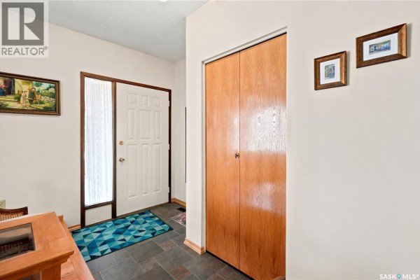 Close-up interior view of a home's entryway, showing a white front door, adjacent window, closet, and carpeted stairs. - 522 Delaronde Road, Saskatoon
