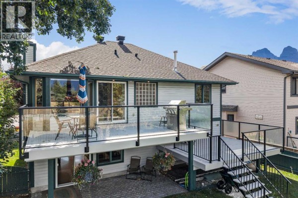 A deck with glass railings and outdoor seating overlooks a backyard and mountains. - 522 Grotto Road, Canmore