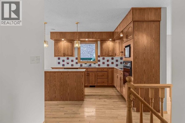 A kitchen features light wood cabinets, a tiled backsplash, and hardwood flooring. - 522 Grotto Road, Canmore