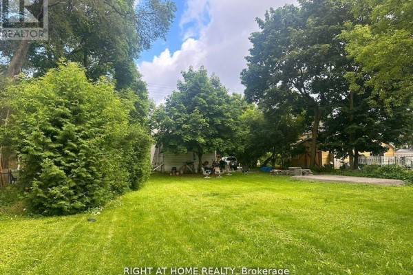 Backyard view of a large grassy area surrounded by mature trees and foliage. - 522 Kingston Road W, Ajax