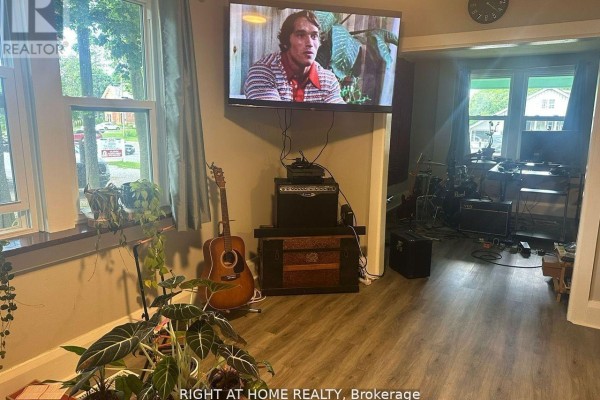 Living room with wood-look vinyl flooring, a wall-mounted television, and a guitar. - 522 Kingston Road W, Ajax