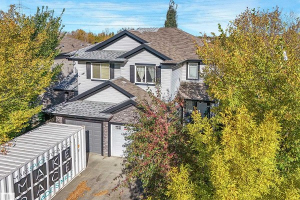 Exterior view of a grey duplex with a garage, large storage container, and fall foliage. - 5220 1a Av Sw, Edmonton