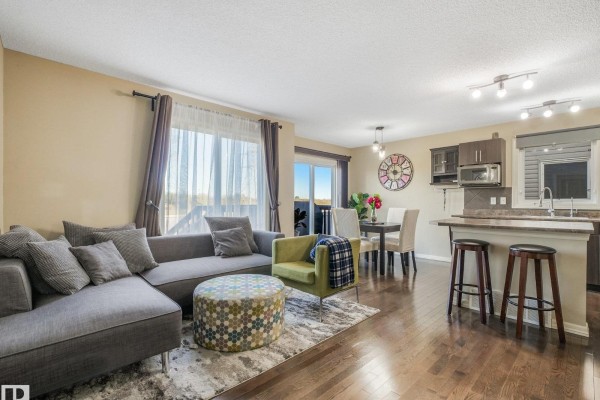 Living room showing a grey sectional sofa, green chair, ottoman, dining table, and kitchen island. - 5220 1a Av Sw, Edmonton