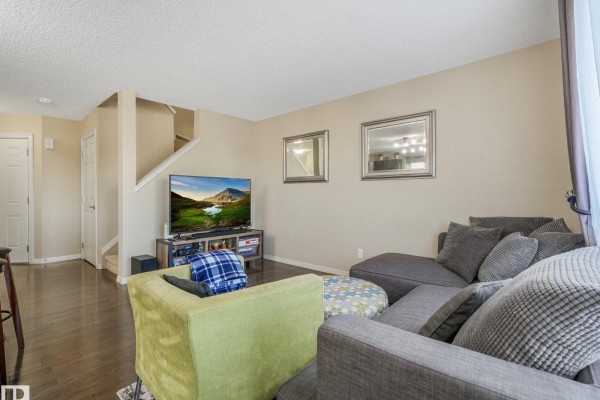 Living room with a grey sectional sofa, green chair, ottoman, and staircase leading to the upper level. - 5220 1a Av Sw, Edmonton