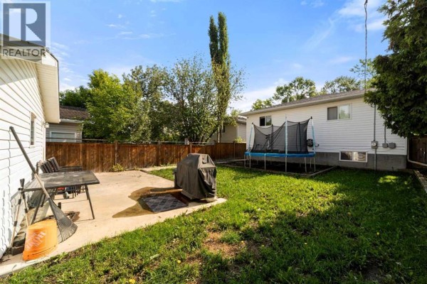 Backyard with a concrete patio, barbecue, trampoline, and wooden fence. - 5224 43 Street, Camrose