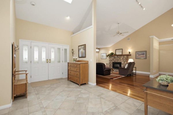 Interior entryway with cream-colored tiled floor and a doorway to a living room with a stone fireplace. - 5226 222 Street, Langley