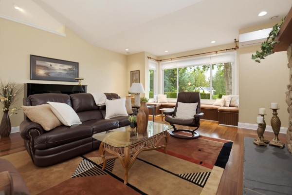 Living room with a large brown leather sectional sofa, glass coffee table, and a window seat. - 5226 222 Street, Langley