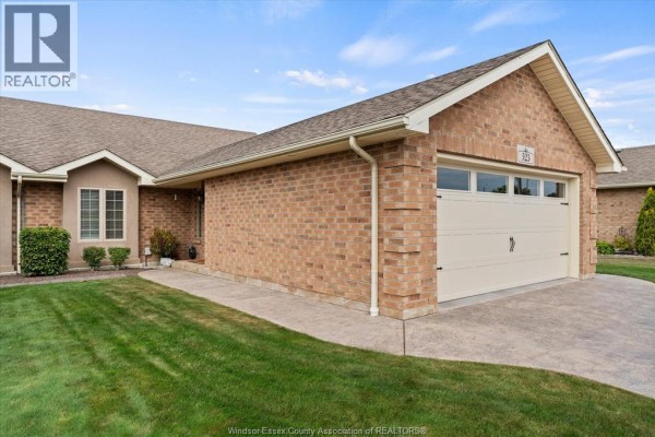 Side view of a brick townhouse with a beige garage door and driveway, with manicured lawn. - 523 Golfview, Amherstburg