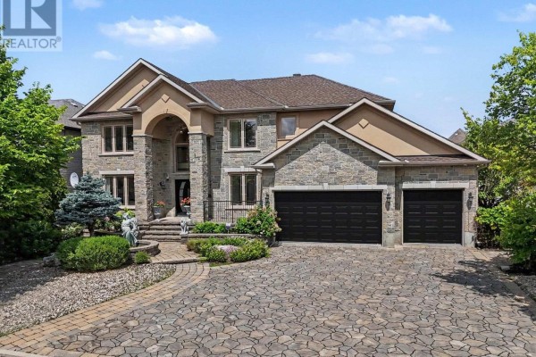 Front view of a large stone house with a multi-car garage and a paved circular driveway. - 523 Kochar Drive, Ottawa