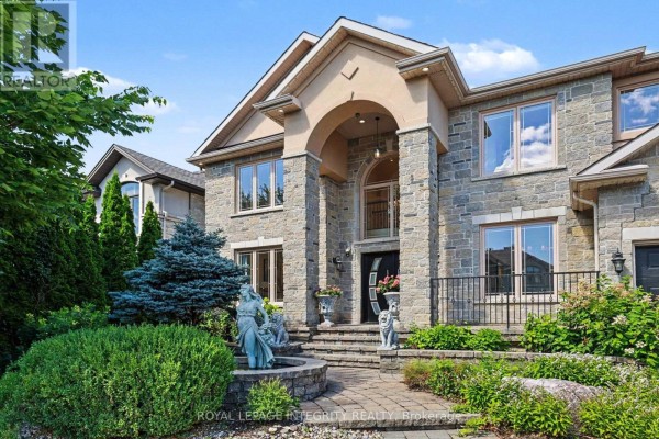 Close-up of the stone facade and arched entryway of a large house with landscaping. - 523 Kochar Drive, Ottawa