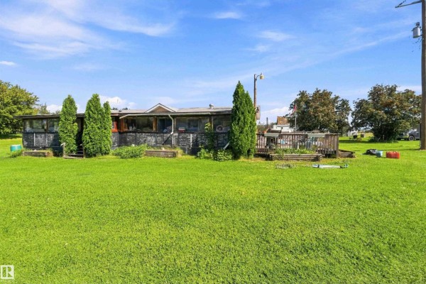Side view of a long, single-story building with a covered porch and surrounding grassy yard. - 52315 Rge Road 273, Rural Parkland County