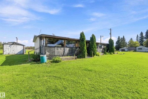 View of the property from the side, showing a screened-in porch and adjacent outbuildings. - 52315 Rge Road 273, Rural Parkland County