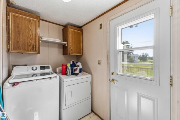 Small laundry room with white washer and dryer, wooden cabinets, and a door with a view of the yard. - 52315 Rge Road 273, Rural Parkland County