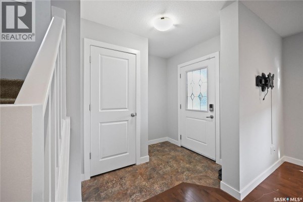 Interior entryway with a white staircase railing, two white doors, and a patterned floor. - 5234 Campling Avenue, Regina