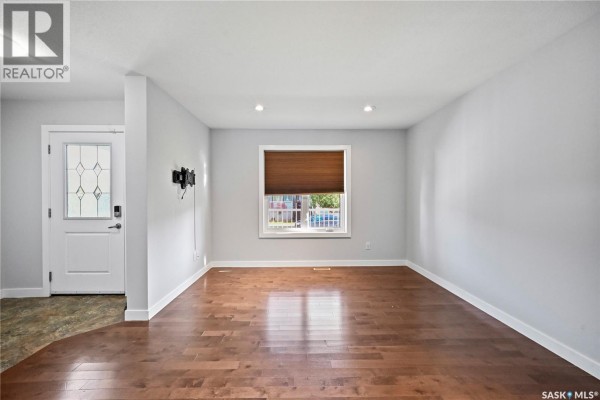 Living room with hardwood floors, grey walls, a window with a slatted blind, and a wall-mounted TV bracket. - 5234 Campling Avenue, Regina