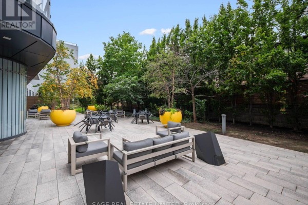Outdoor patio area with seating, tables, and yellow planters surrounded by trees. - 524 - 38 Cameron Street, Toronto