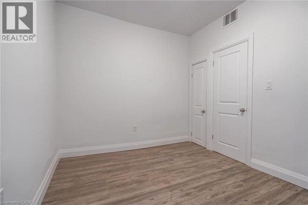 Empty room with white walls, wood-look laminate flooring, and two white doors. - 524 King Street E Unit# 3, Hamilton