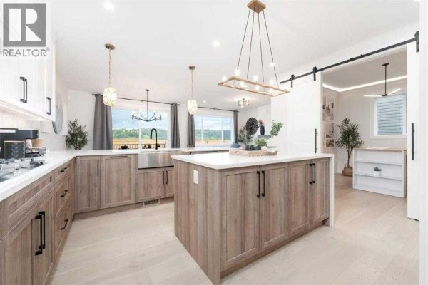 Modern kitchen with light wood cabinets, white countertops, island, stainless steel sink, and view to backyard. - 524 Waterford Grove, Chestermere