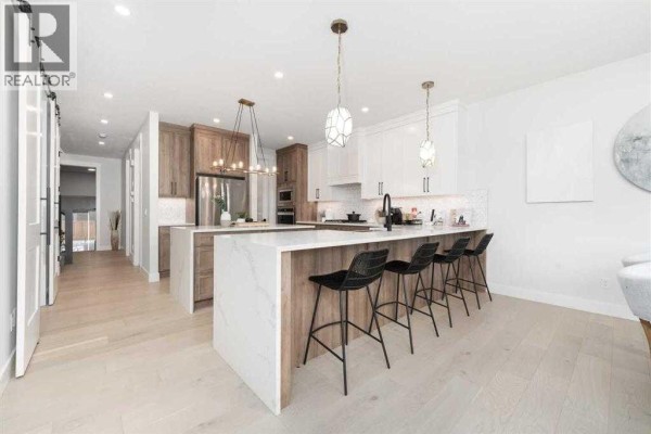 Spacious kitchen with two islands, white cabinets, wood-look lower cabinets, and seating at the island. - 524 Waterford Grove, Chestermere