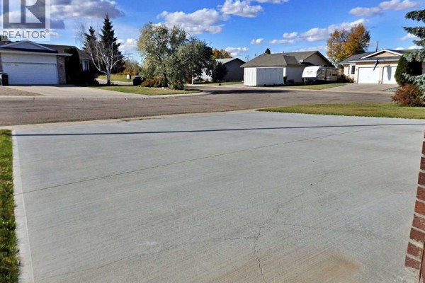 Concrete driveway facing houses on a quiet street with scattered trees and blue sky. - 5243 66 Street, Vermilion