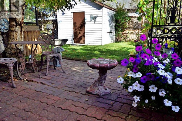 Paved backyard patio with a bird bath, metal table and chairs, and a white shed. - 5243 66 Street, Vermilion