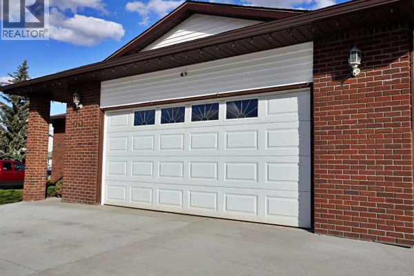 White garage door with decorative glass panes, surrounded by red brick exterior walls. - 5243 66 Street, Vermilion