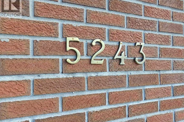 Brass house numbers '5243' mounted on a rough textured red brick exterior wall. - 5243 66 Street, Vermilion