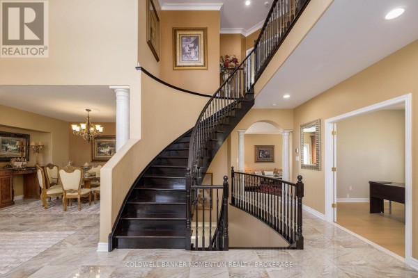 Curved dark wood staircase with black railings ascends from a tiled foyer with an arched doorway. - 5246 Marcel Crescent, Niagara Falls