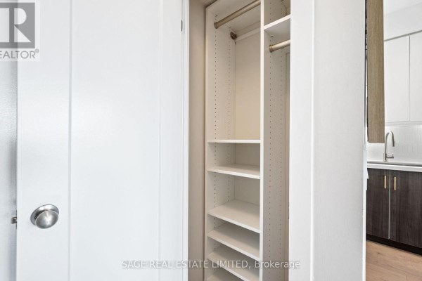 Open closet with white shelves and metal hanging rods, next to kitchen cabinets. - 525 - 8 Fieldway Road, Toronto