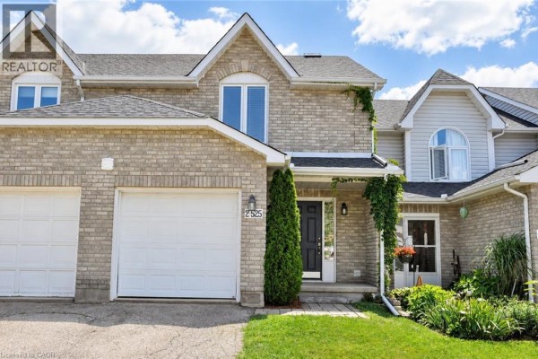 Exterior of a beige brick townhouse with a two-car garage and white garage doors. - 525 Oakvale Drive Unit# 2, Waterloo
