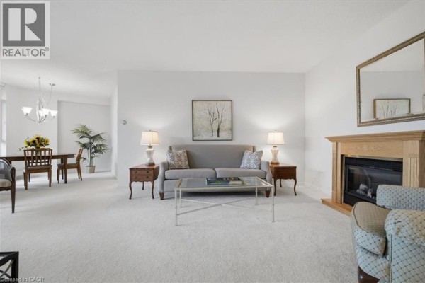 Living room with a grey sofa, glass coffee table, fireplace, and dining area in background. - 5250 Lakeshore Road Unit# 401, Burlington