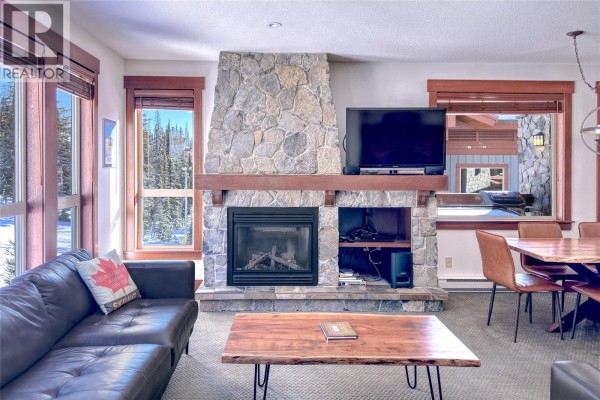 Living and dining area with a stone fireplace, wooden table, and kitchen island. - 5257 Big White Road Unit# 306, Big White