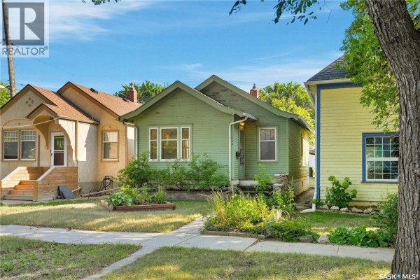 Exterior of a light green wood-sided house with surrounding houses and trees. - 526 7th Street E, Saskatoon