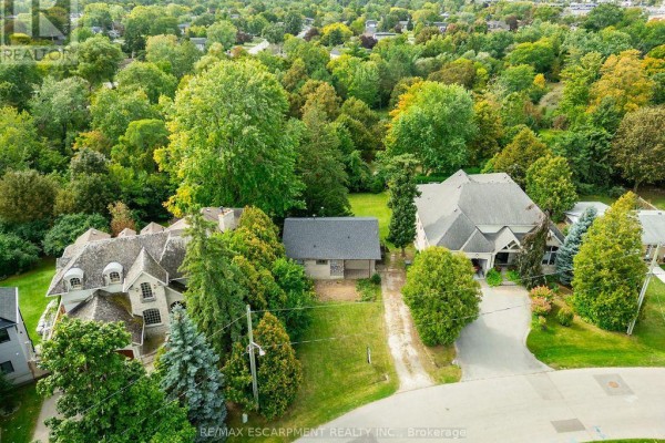 Aerial view of three homes on tree-lined lots, including a grey stone house with a mansard roof. - 526 Stafford Drive, Oakville