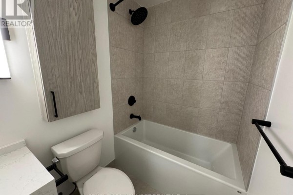 Close-up of bathroom with beige tiled walls, white tub, toilet, and vanity. - 527 - 91 Montclair Avenue, Toronto