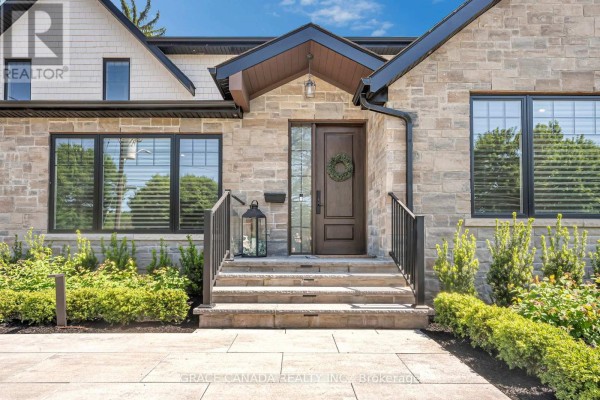 Close-up of the front entrance with stone facade, wooden door, glass sidelights, and stone steps. - 527 Oneida Drive, Burlington