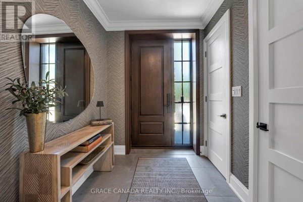 Interior entryway with a dark wood door, patterned wallpaper, round mirror, console table, and grey rug. - 527 Oneida Drive, Burlington