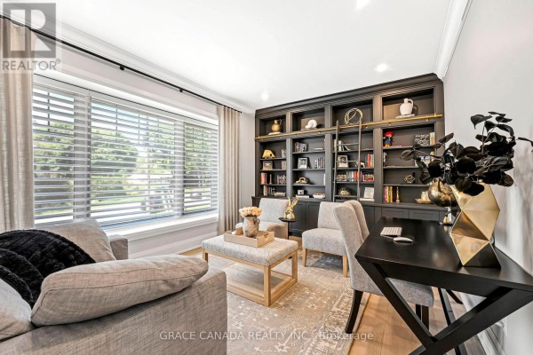 Home office with a large window, grey sofa, ottoman, desk, and a dark grey built-in bookshelf with a ladder. - 527 Oneida Drive, Burlington