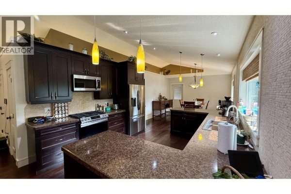 Kitchen with dark cabinetry, stainless steel appliances, and a granite countertop island. - 5276 Chintu Drive, 108 Mile Ranch