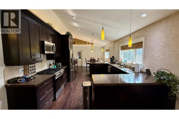 Spacious kitchen layout with pendant lighting, large windows, and a view of the dining area. - 5276 Chintu Drive, 108 Mile Ranch