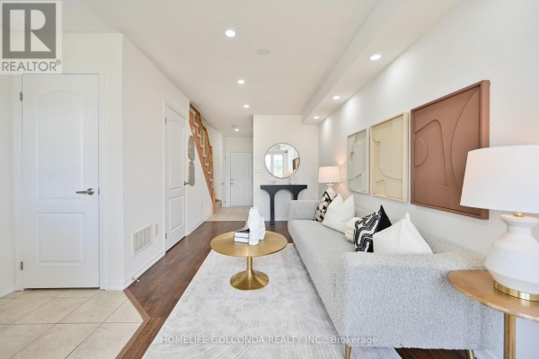 Living room with a sofa, coffee table, and entryway leading to stairs. - 5277 Major Mackenzie Drive E, Markham