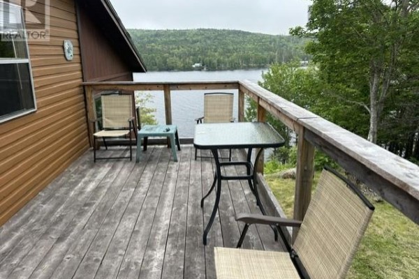 Deck with table and chairs overlooking a calm lake and forested hills. - 528 West Side Indian Harbour Lake Road, Indian Harbour Lake