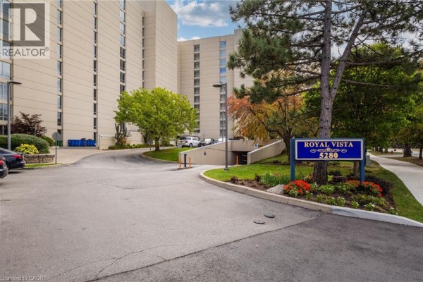 Entrance to the Royal Vista apartment building with a sign and underground parking ramp. - 5280 Lakeshore Road Unit# 103, Burlington