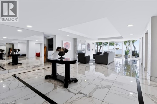 Spacious, modern lobby with marble tile floors, seating area, and large windows overlooking water. - 5280 Lakeshore Road Unit# 103, Burlington