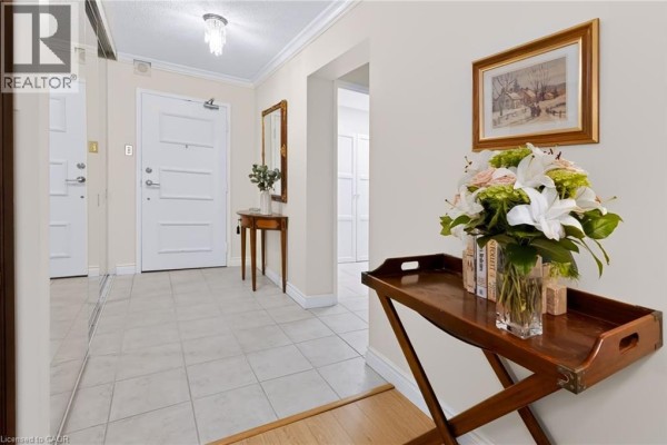 Hallway leading to apartment door with a wooden console table and floral arrangement. - 5280 Lakeshore Road Unit# 103, Burlington