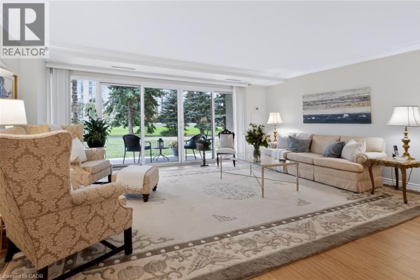 Living room with beige furniture, large rug, fireplace, and sliding glass doors to a patio. - 5280 Lakeshore Road Unit# 103, Burlington